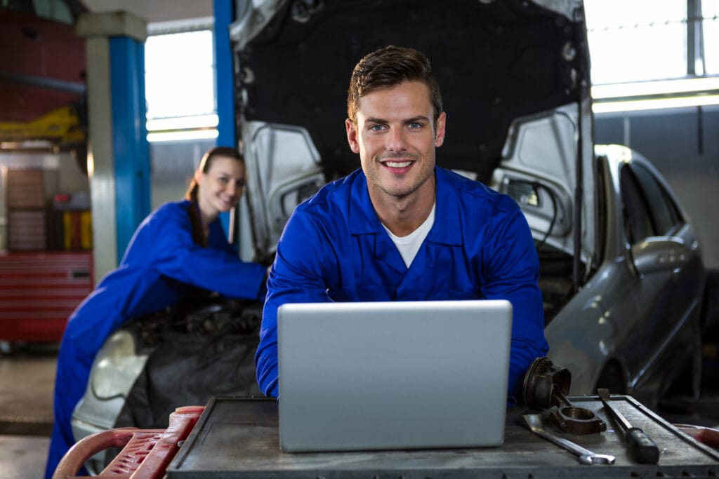 Portrait of happy mechanic working on laptop at repair garage